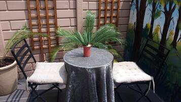 Un petit espace extérieur aménagé avec deux chaises et une table, un pot de fleurs et une fresque murale.