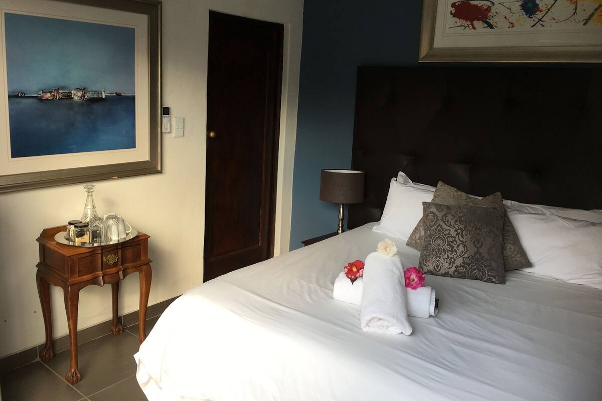 Une chambre d’hôtel avec un lit, une table de chevet, une lampe, un tableau et une porte.