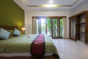 A hotel room with a large bed, a nightstand, a lamp, a wardrobe, and a view of greenery through the window. - Umah Diuma (Ubud)