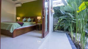 A bedroom with a bed, bedside table, and a view of a garden. - Umah Diuma (Ubud)