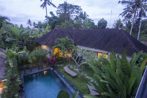 A traditional house with a tiled roof, surrounded by lush tropical vegetation and a swimming pool. - Umah Diuma (Ubud)