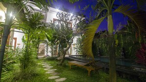 A well-lit garden with a pathway, palm trees, and a bench. - Umah Diuma (Ubud)