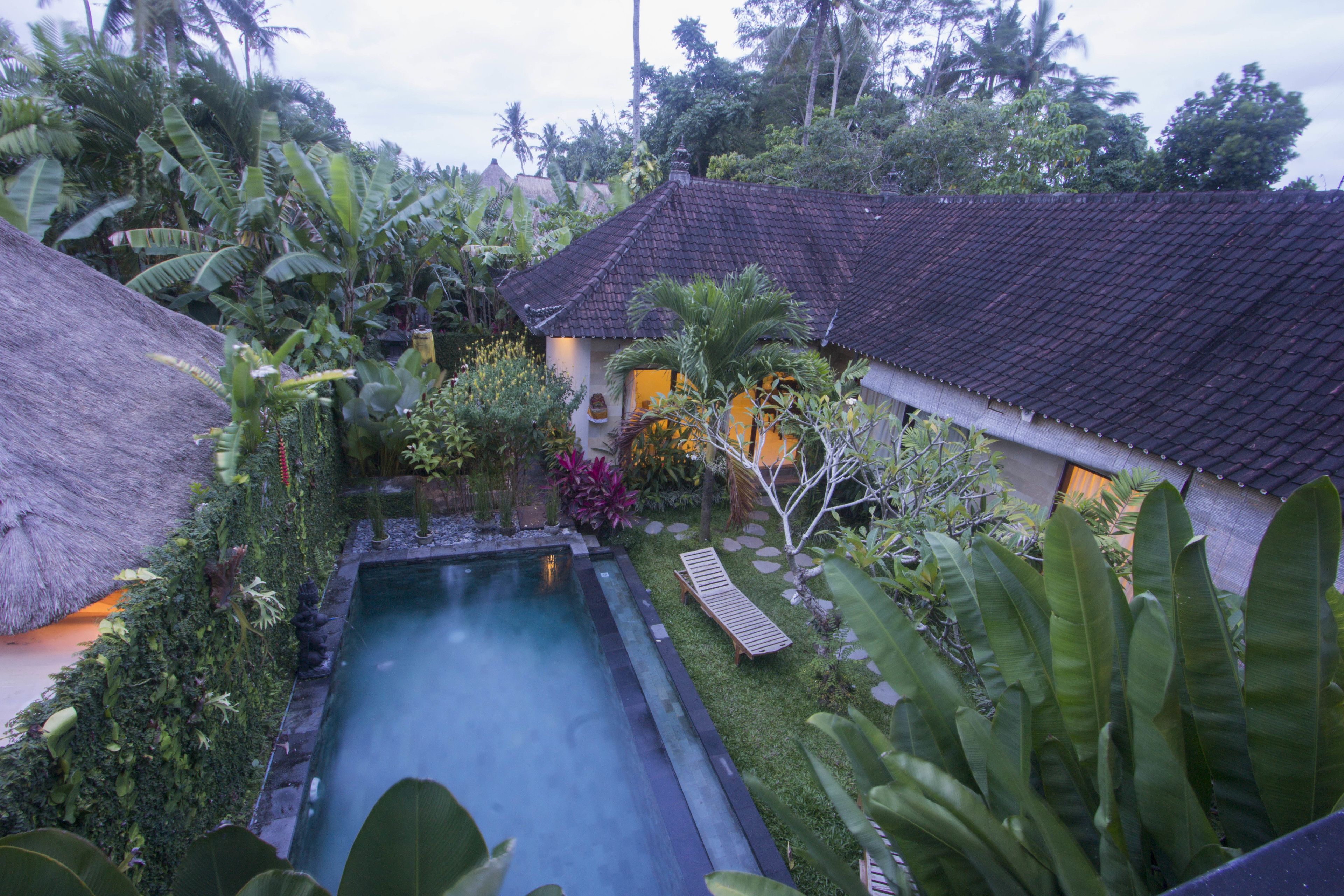 Una casa tradizionale con tetto di paglia e una piscina circondata da rigogliosa vegetazione tropicale.