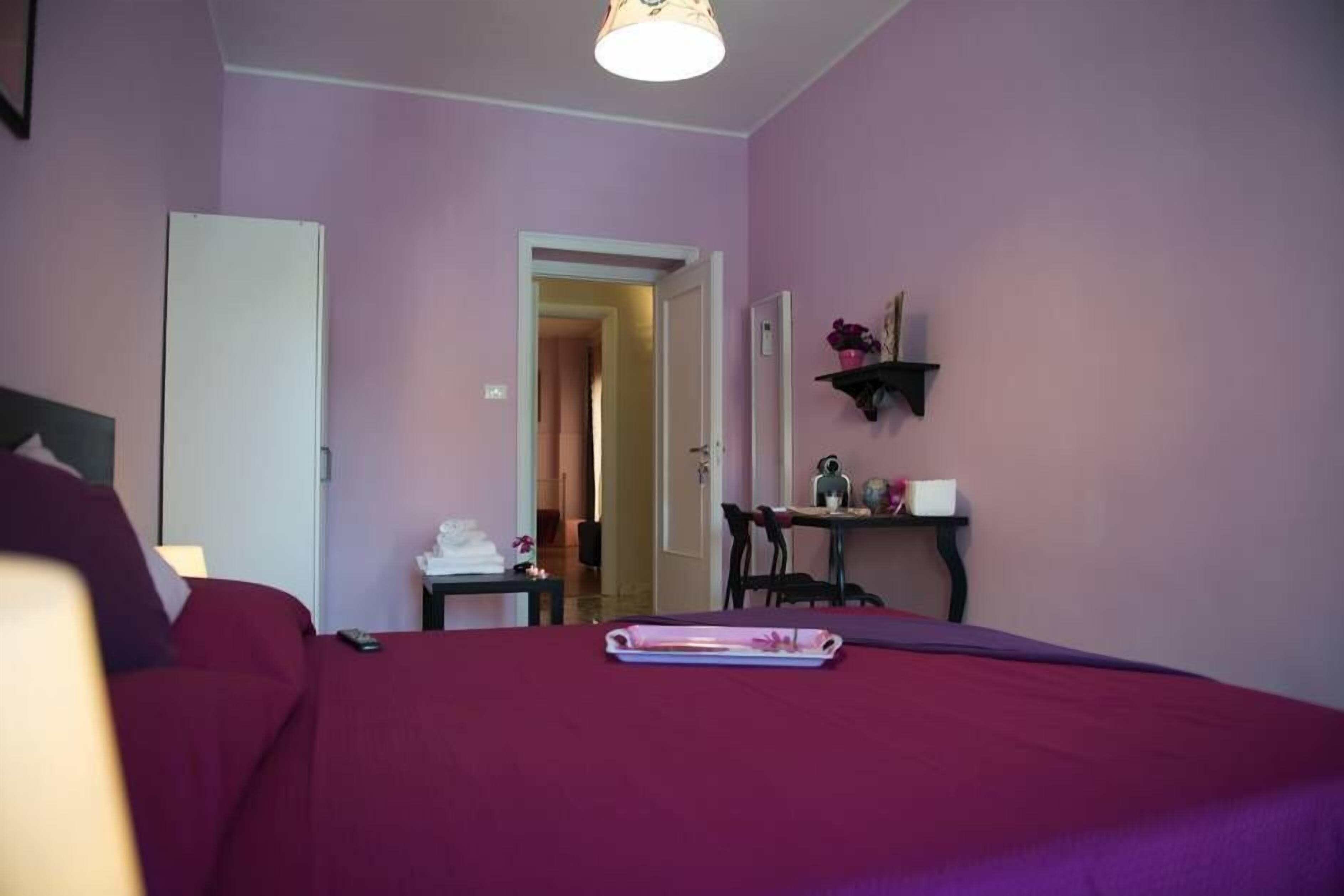 A bedroom with a bed, a nightstand, a chair, and a desk with a lamp.