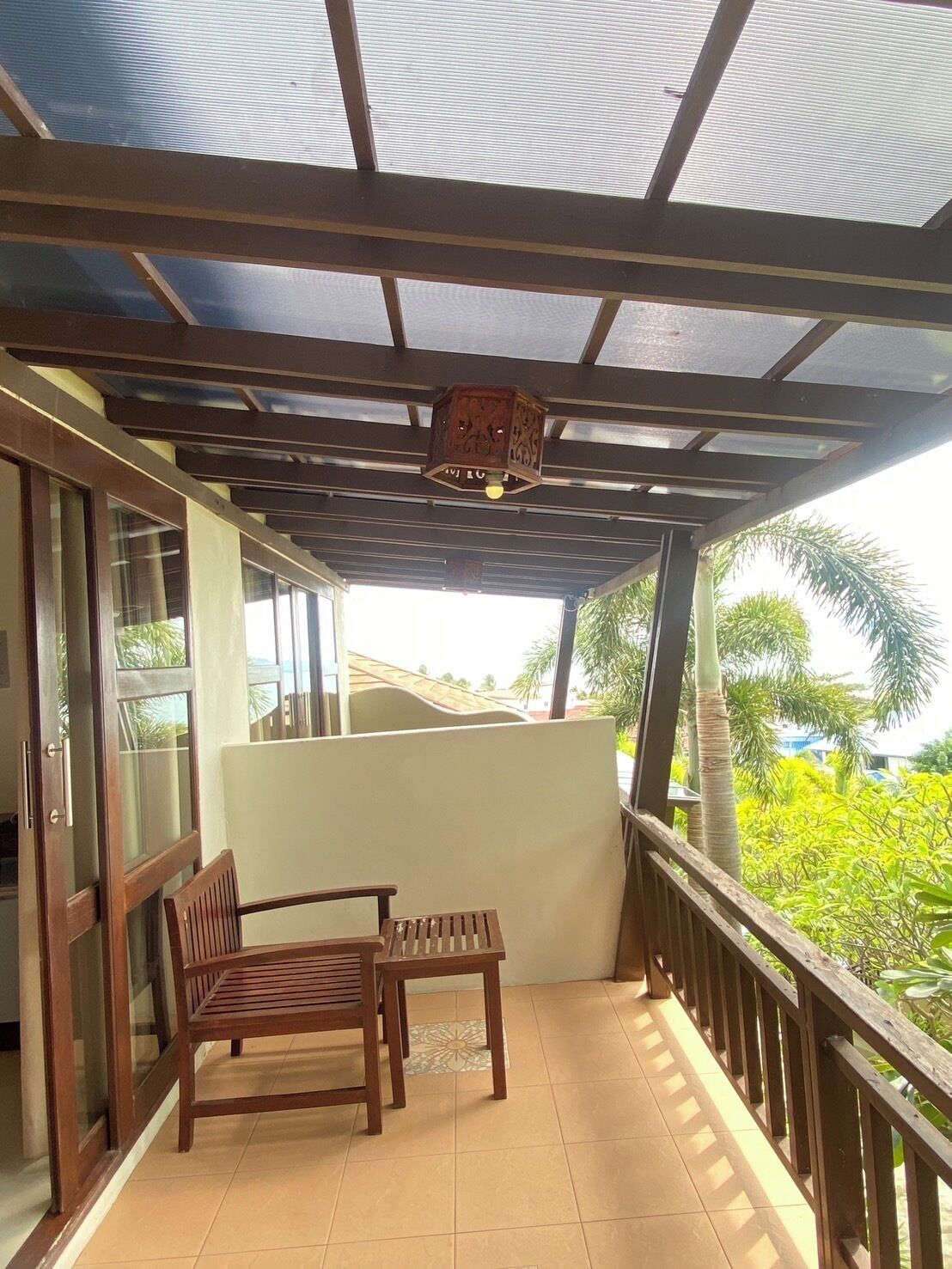 A covered balcony with wooden furniture, a ceiling light fixture, and a view of greenery outside.