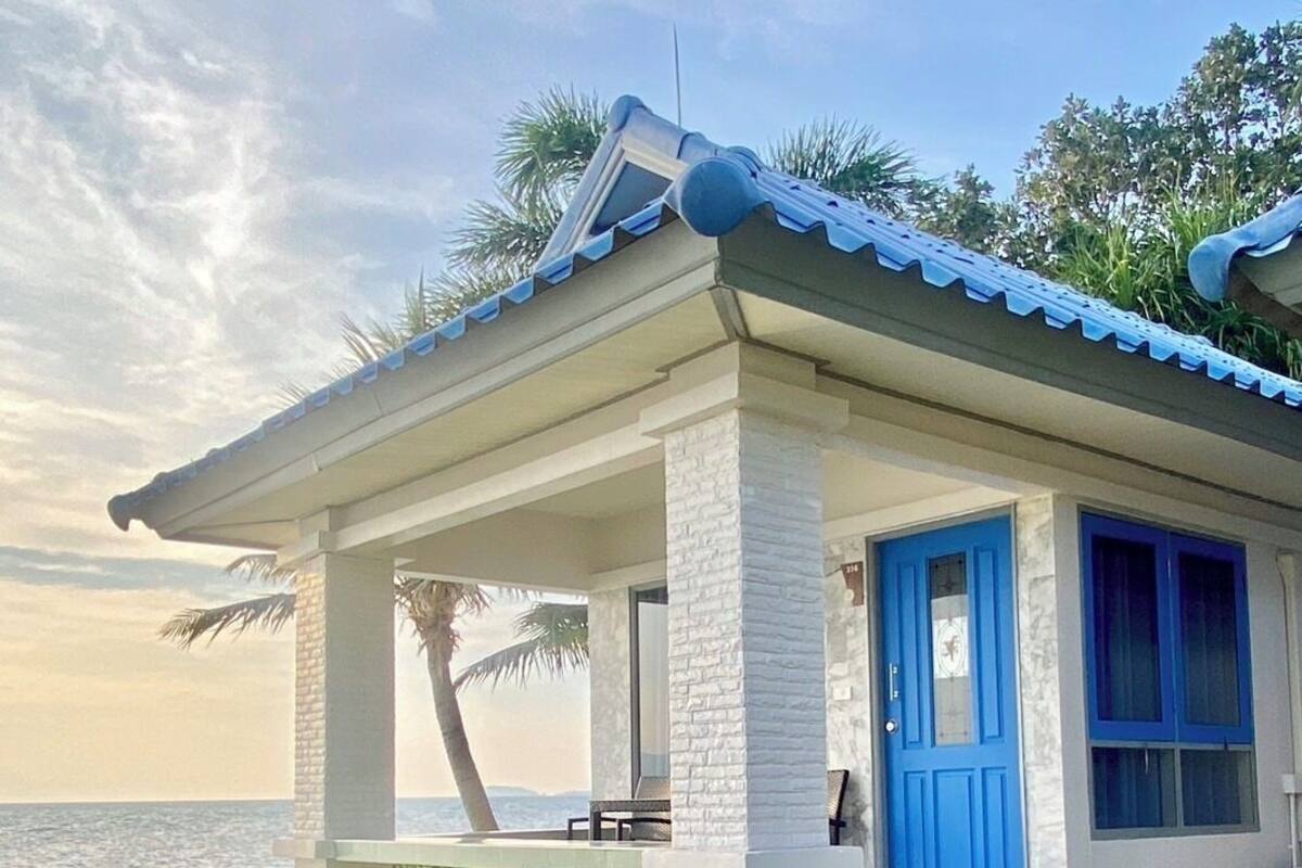 A coastal house with a blue door, white walls, and a tiled roof.