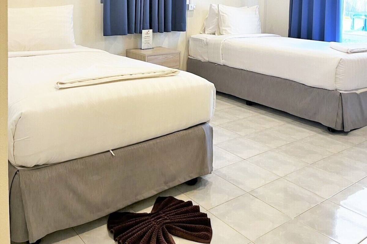 A hotel room with two beds, a nightstand, and a large window with blue curtains.