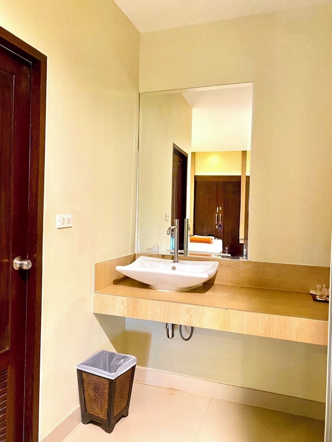 Un baño con un espejo grande, un lavamanos y un cubo de basura.