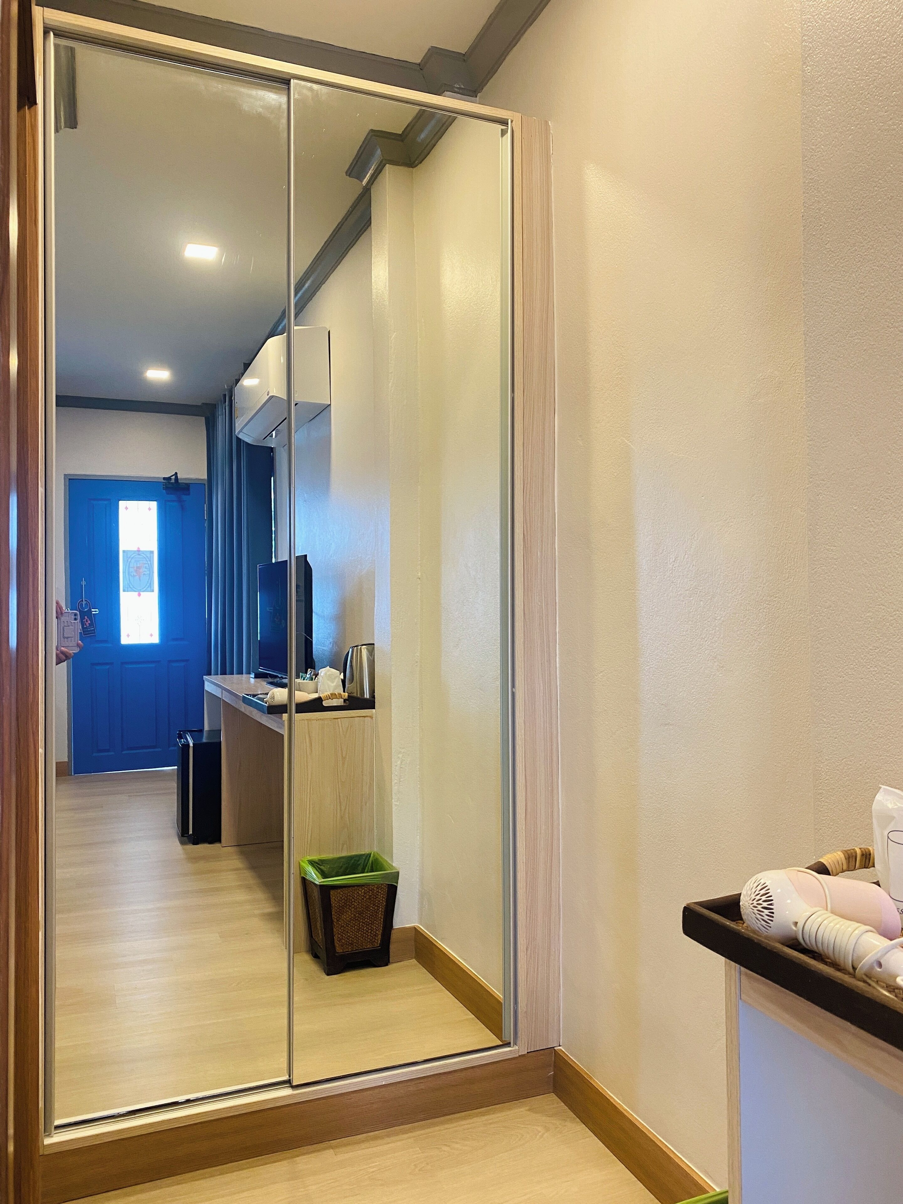 Un couloir avec une porte de placard à miroir, une porte bleue au fond et une petite poubelle.