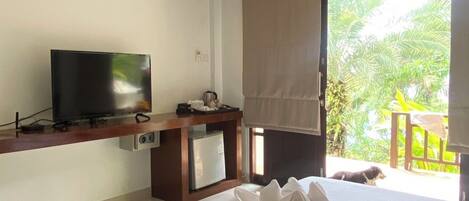 A hotel room with a bed, a TV, a minibar, and a view of the outdoors.