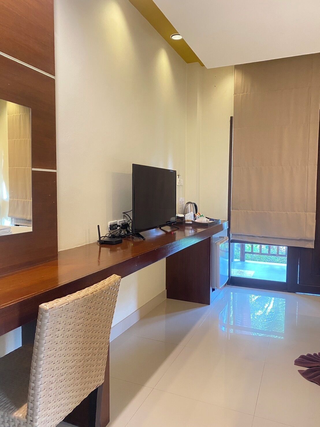 A modern hotel room with a wooden desk, a flat-screen TV, a coffee maker, and a large window with a view of the outdoors.