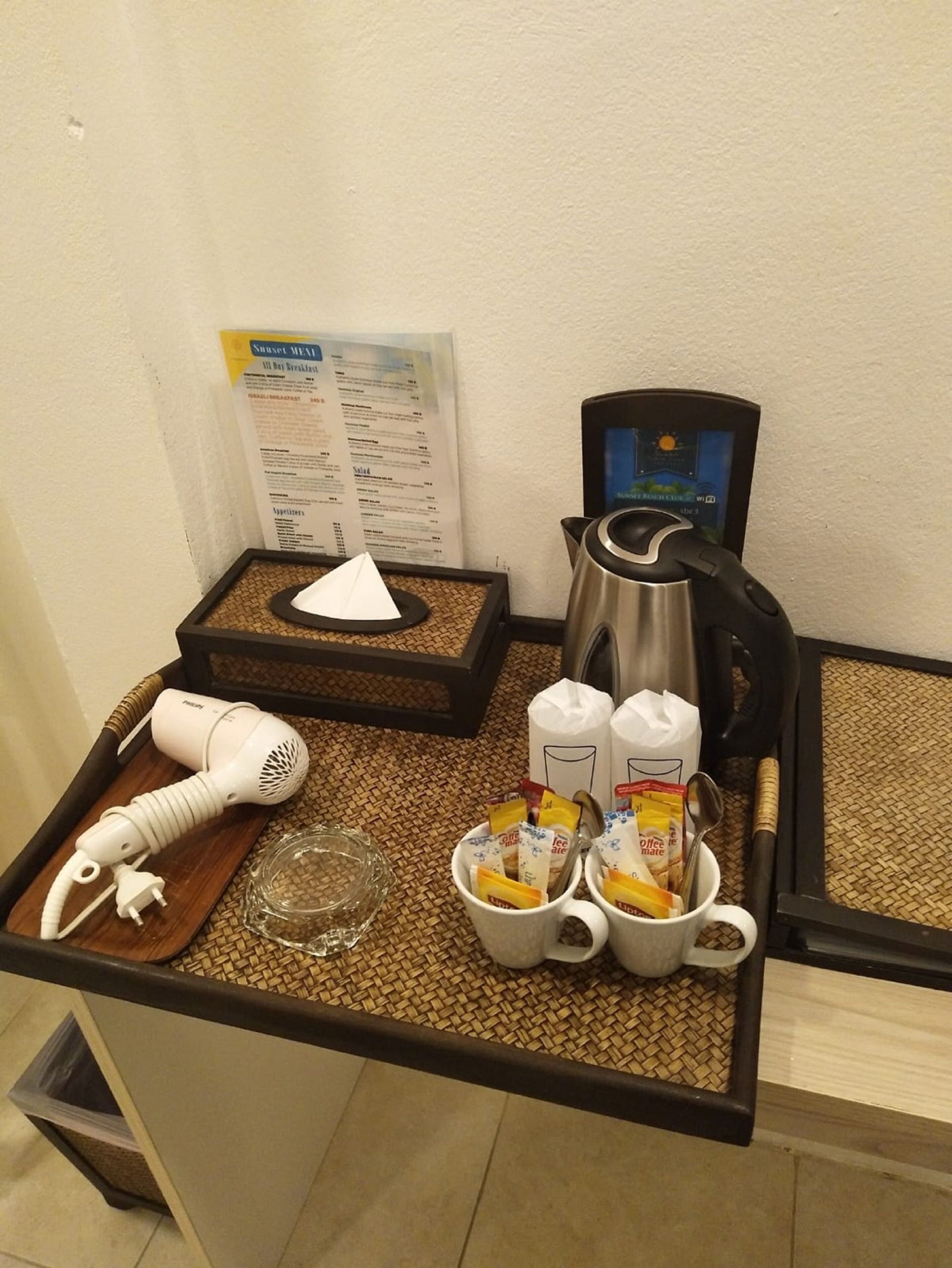A hotel room's breakfast area with a hairdryer, coffee maker, and a menu on the wall.