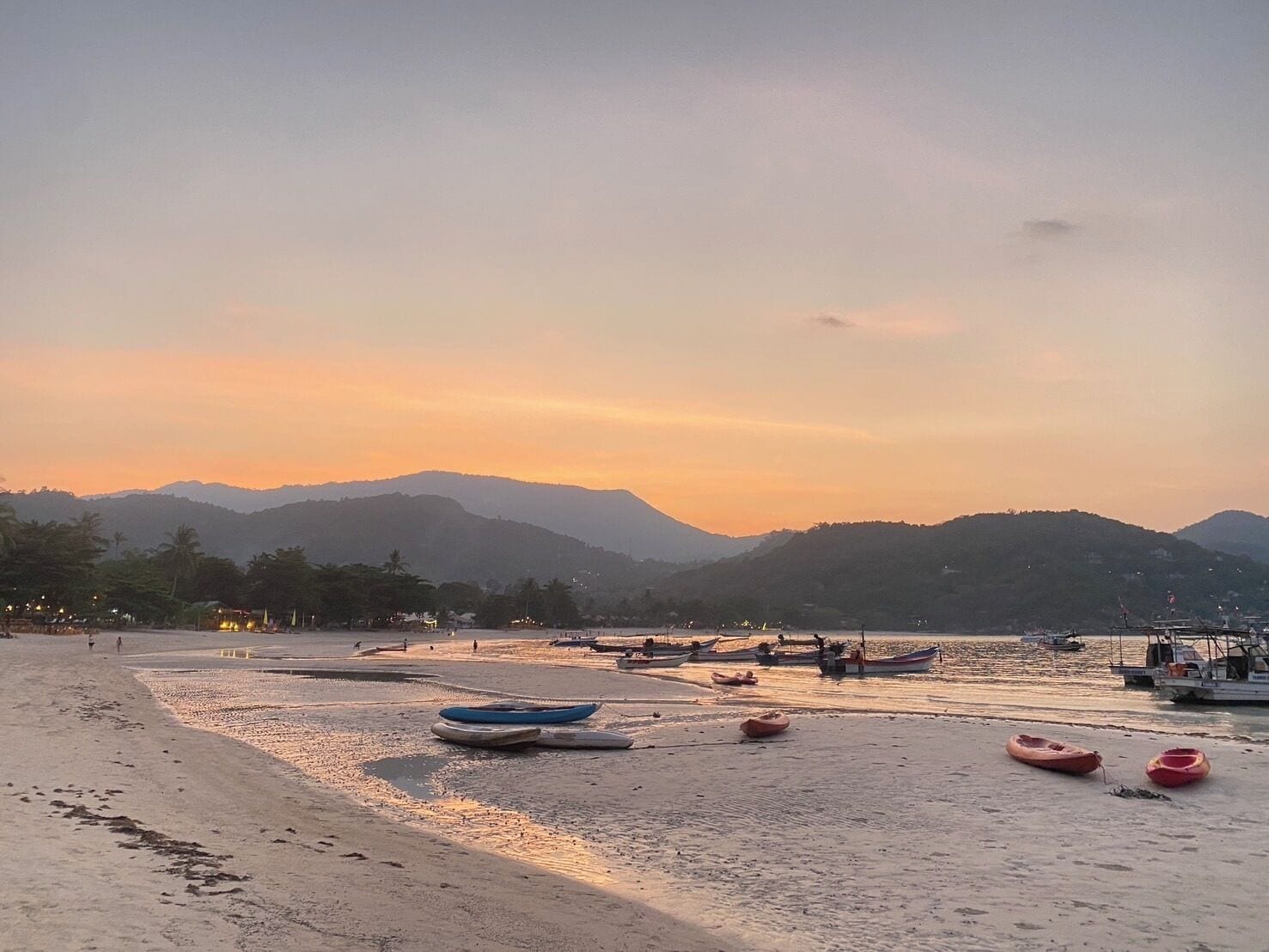 A beach with boats and a mountainous backdrop during sunset.