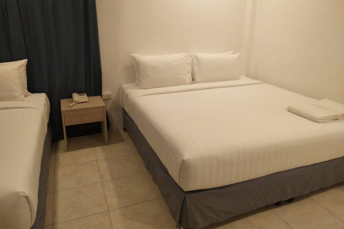 A hotel room with a bed, a bedside table with a phone, and a curtain.