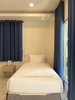 Cama bem arrumada com lençóis brancos, mesa de cabeceira de madeira com um objeto em cima e janela com cortinas azuis.