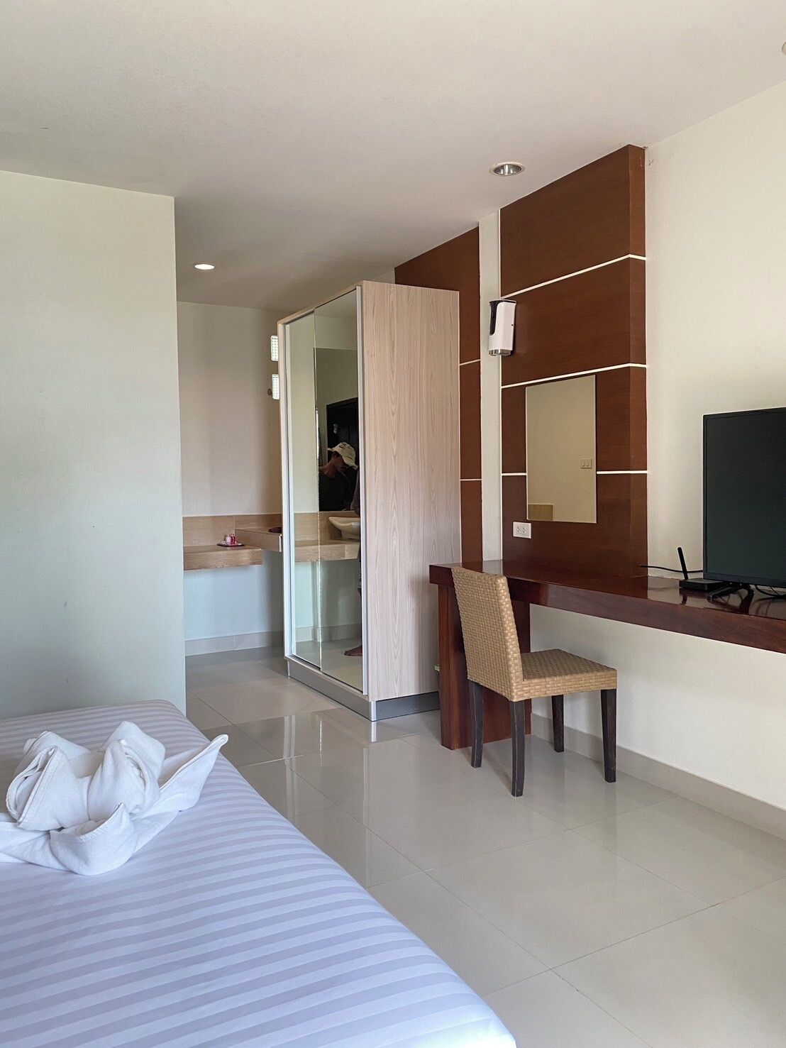A hotel room with a bed, a desk with a chair, a mirror, and a television.