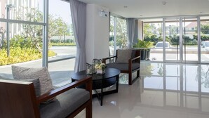 A modern hotel lobby with large windows, a seating area with sofas and a coffee table, and a view of the parking area. - Marine Room At Baan Khun Koey Hua Hin (Hua Hin)