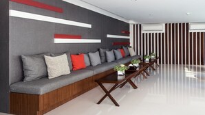 A modern waiting area with a grey sofa, red and white cushions, wooden tables, and a striped wall. - Marine Room At Baan Khun Koey Hua Hin (Hua Hin)