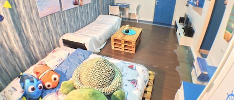 A room with a bed, a small table, a desk, and a chair. There are wall decorations and a door.