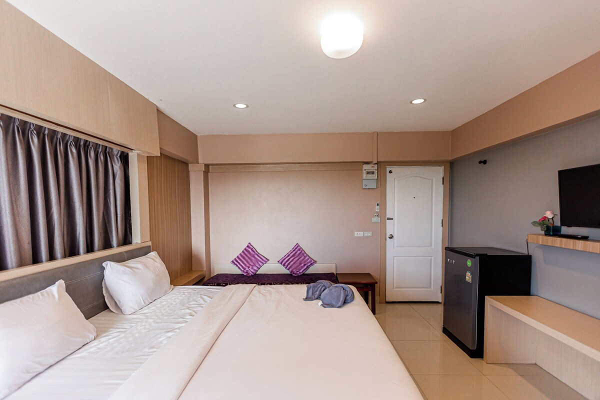 A hotel room with a bed, a desk, a television, and a refrigerator.