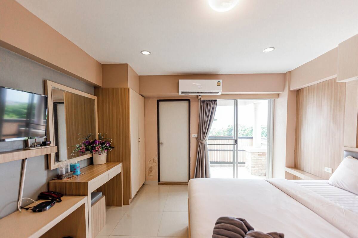 A hotel room with a bed, a TV, a desk, a wardrobe, and a balcony.