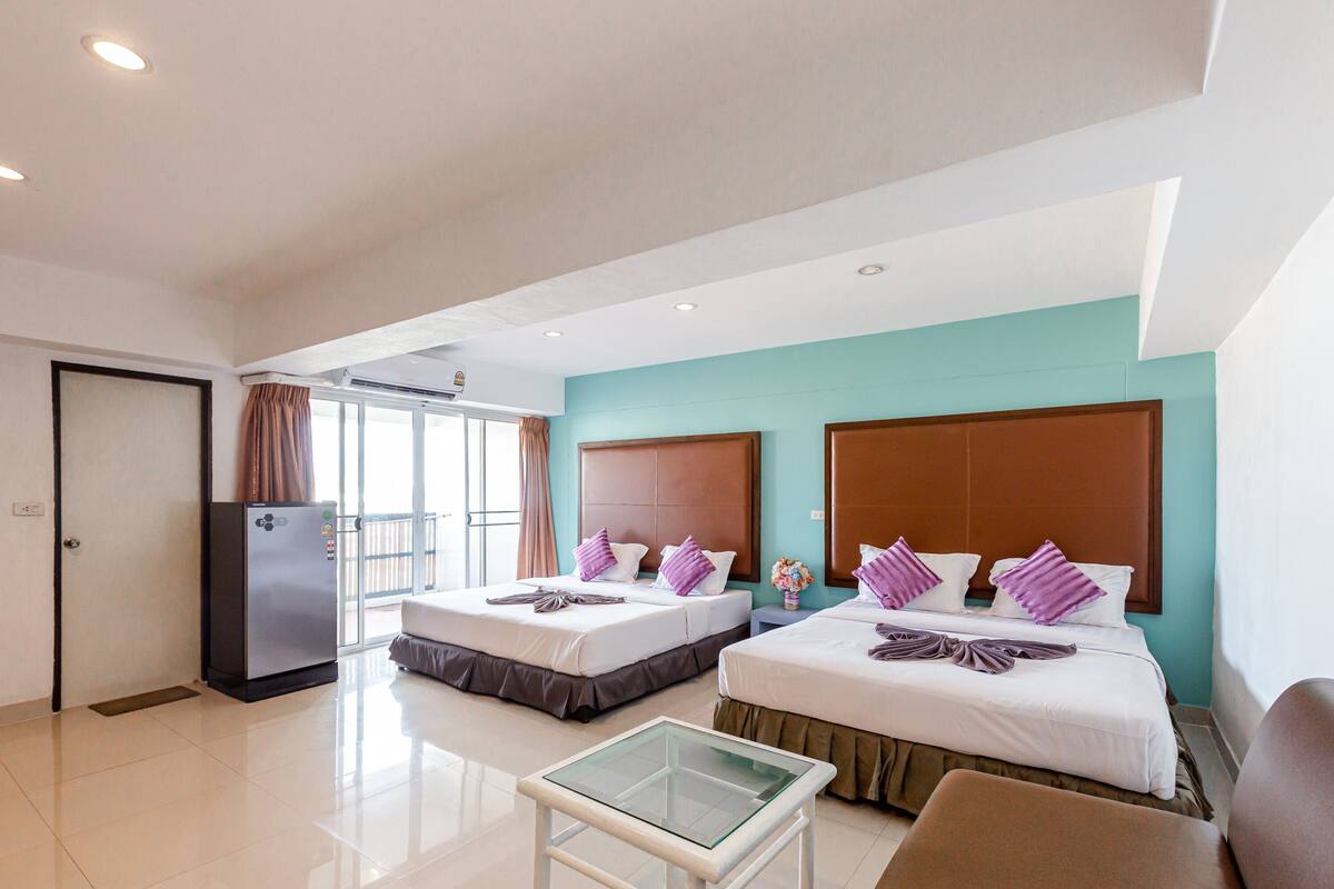 Een hotelkamer met twee bedden, een koelkast, een glazen bijzettafeltje en een bank.