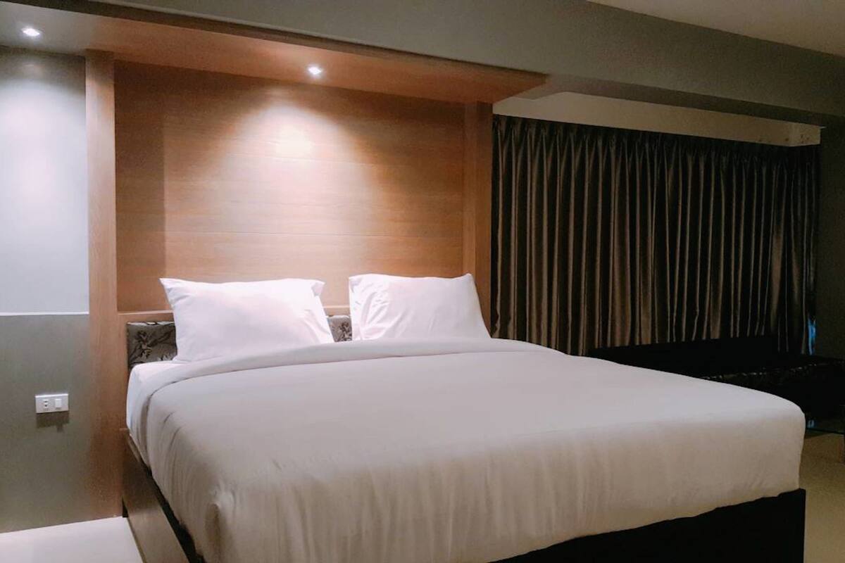 Een moderne hotelkamer met een groot bed, een houten hoofdbord en een donkere gordijnen achtergrond.