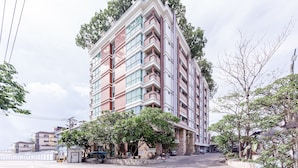 A multi-story hotel with balconies, a parking area, and surrounding greenery. - Latin Garden (Bangkok)