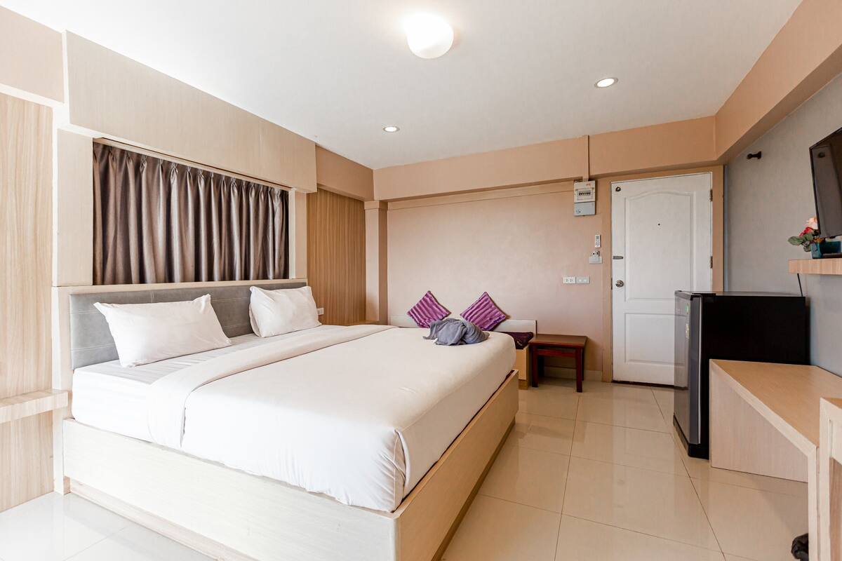 A hotel room with a large bed, a desk with a computer, a door, and a small table.