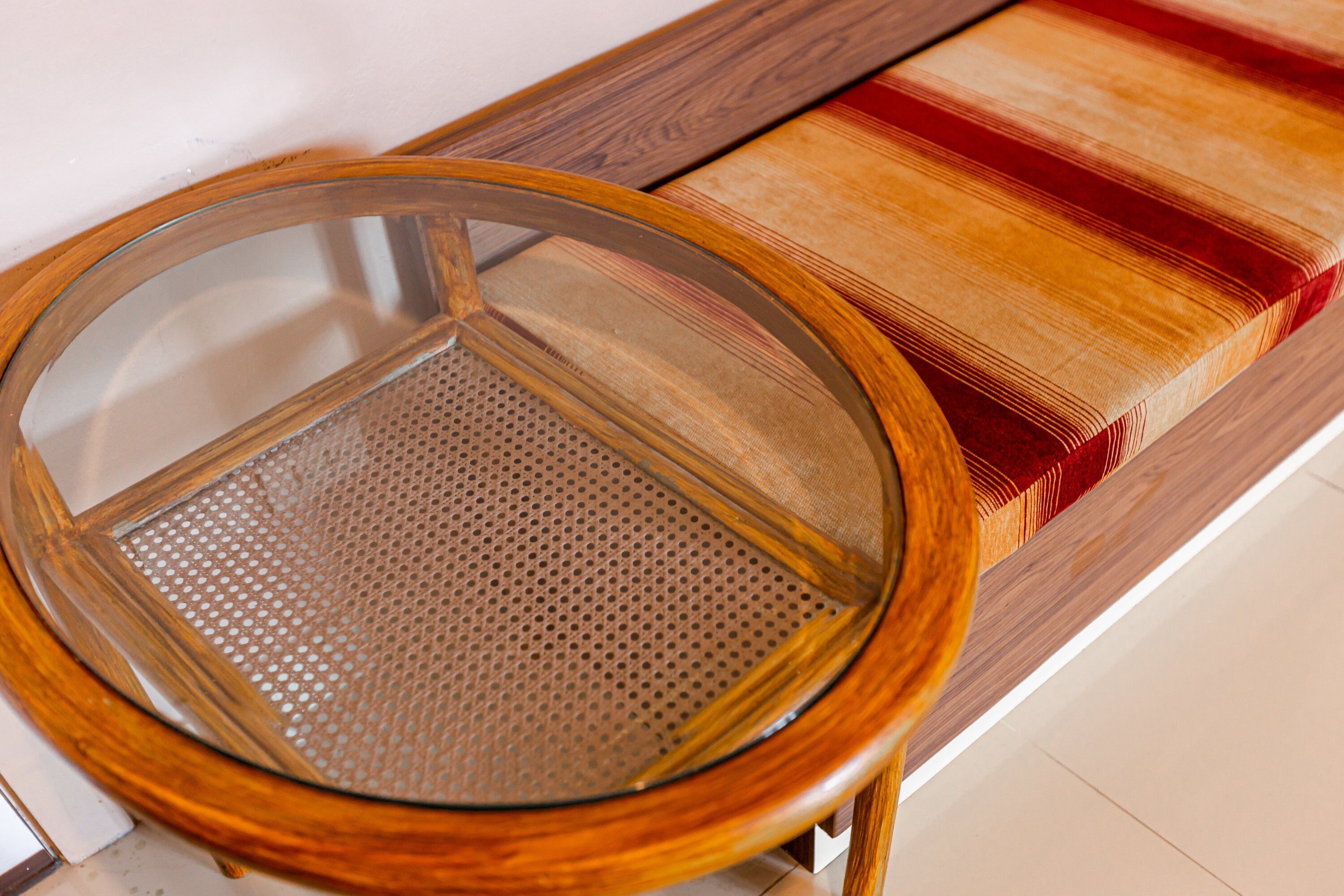 A round wooden table with a glass top and a perforated metal base.
