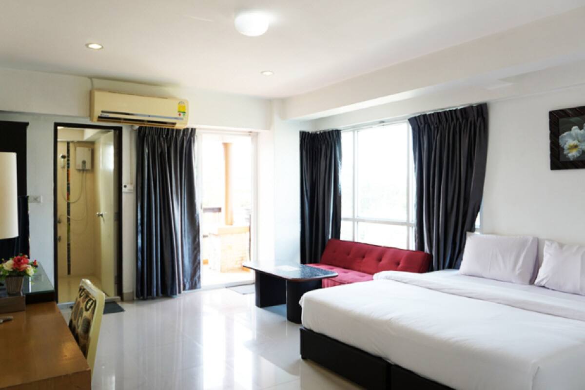 Een hotelkamer met een bed, een rode bank, een tafeltje en een raam met gordijnen.