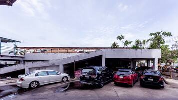 A parking area with multiple cars, a covered structure, and a building with a flat roof.