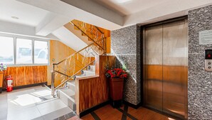 A modern elevator with a granite wall and a wooden staircase with metal railings. - Latin Garden (Bangkok)