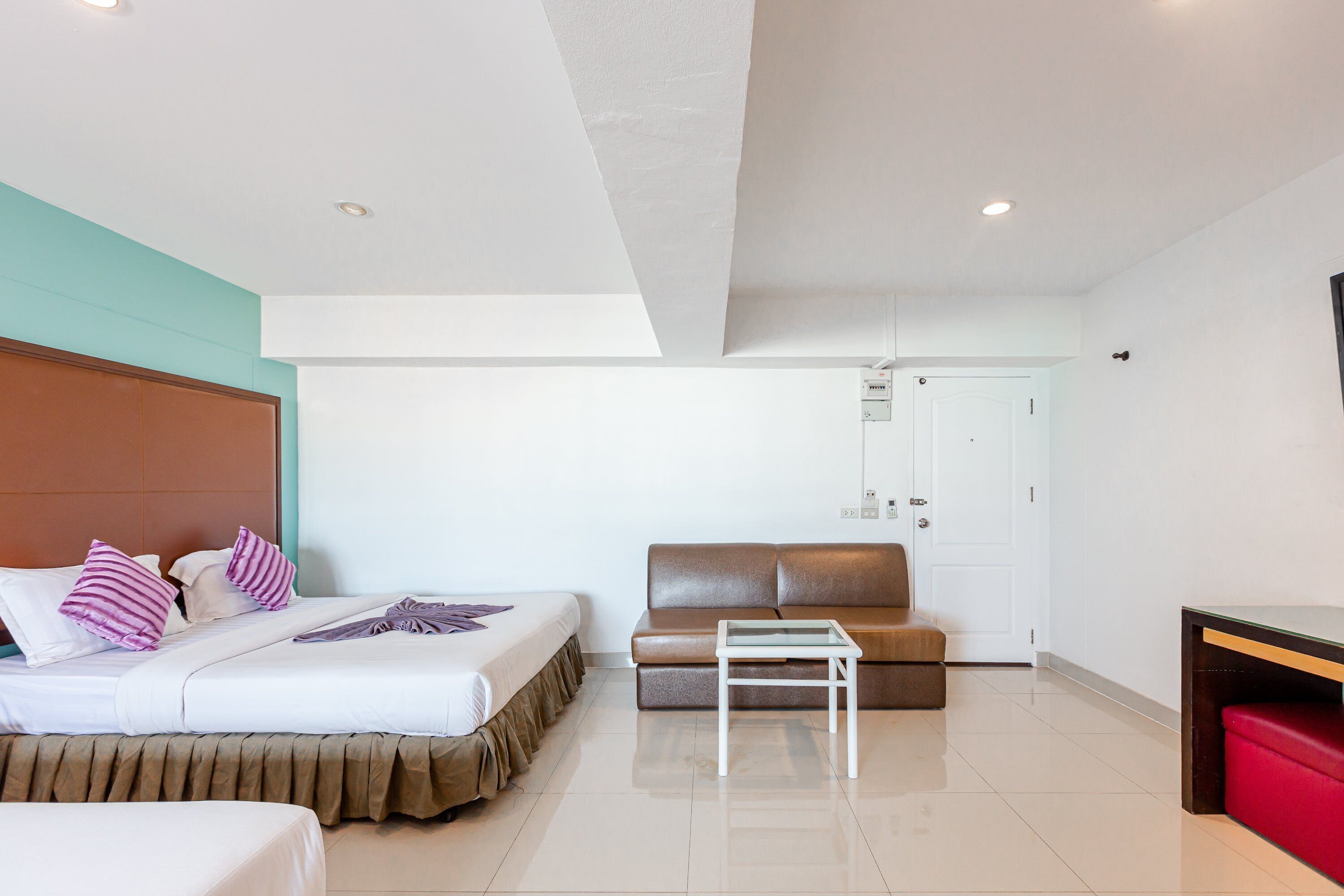 A hotel room with a bed, a sofa, a small table, and a red bench.