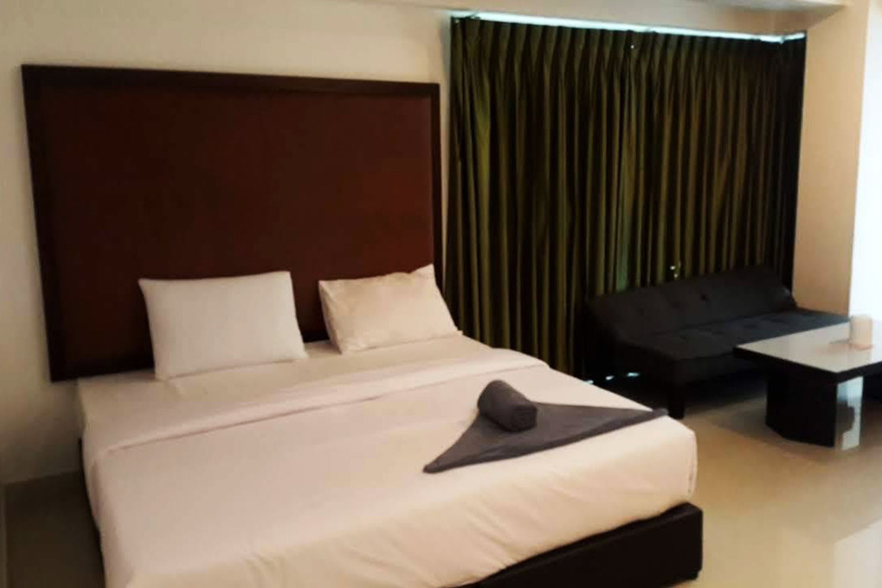 A hotel room with a large bed, a dark-colored headboard, a black sofa, and a small table with a cup.