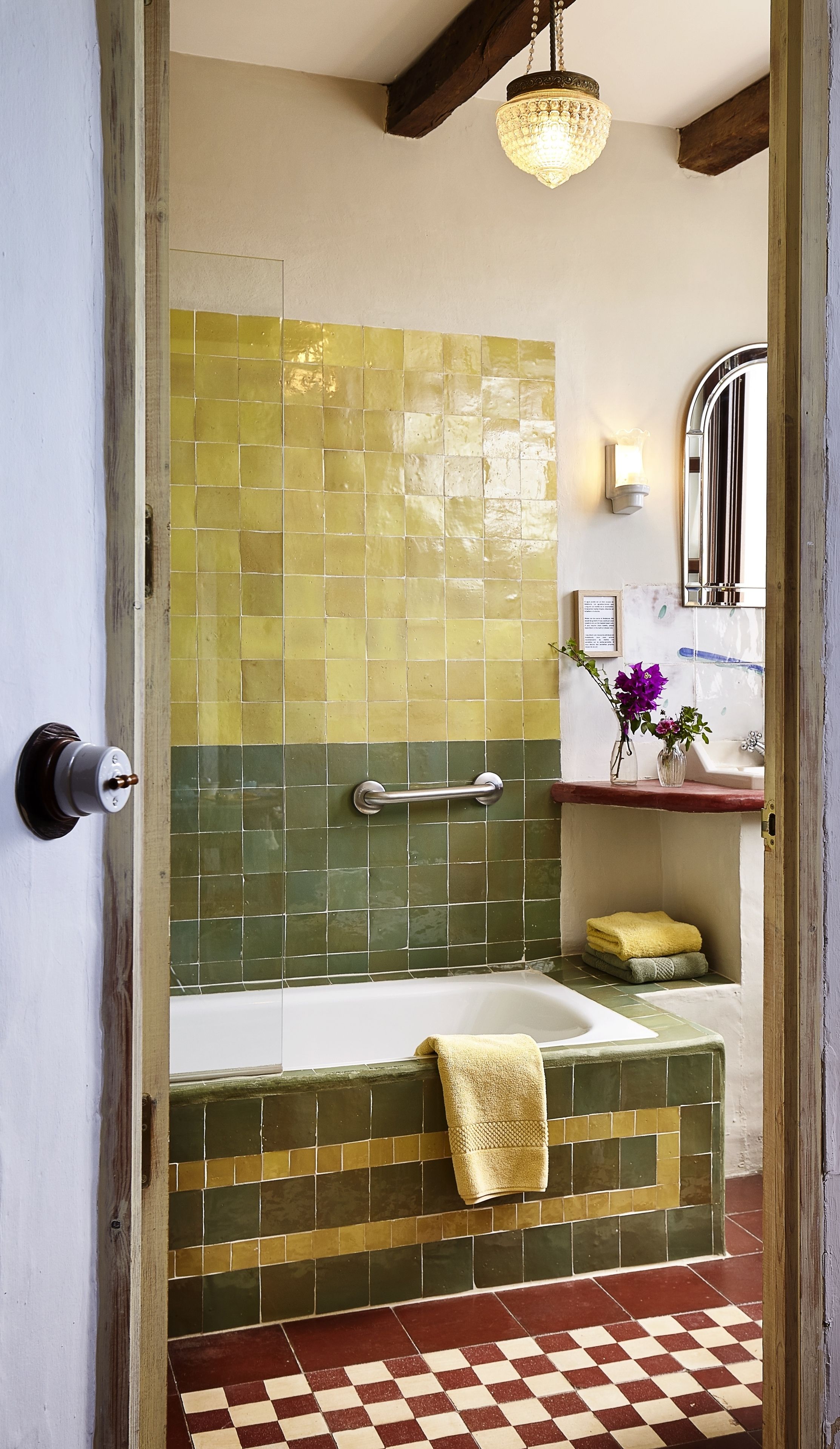 A bathroom with a checkered floor, a bathtub, a handrail, and a mirror.
