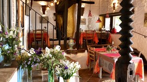 Un comedor rústico con mesas y sillas de madera, una escalera y lámparas esféricas colgantes.