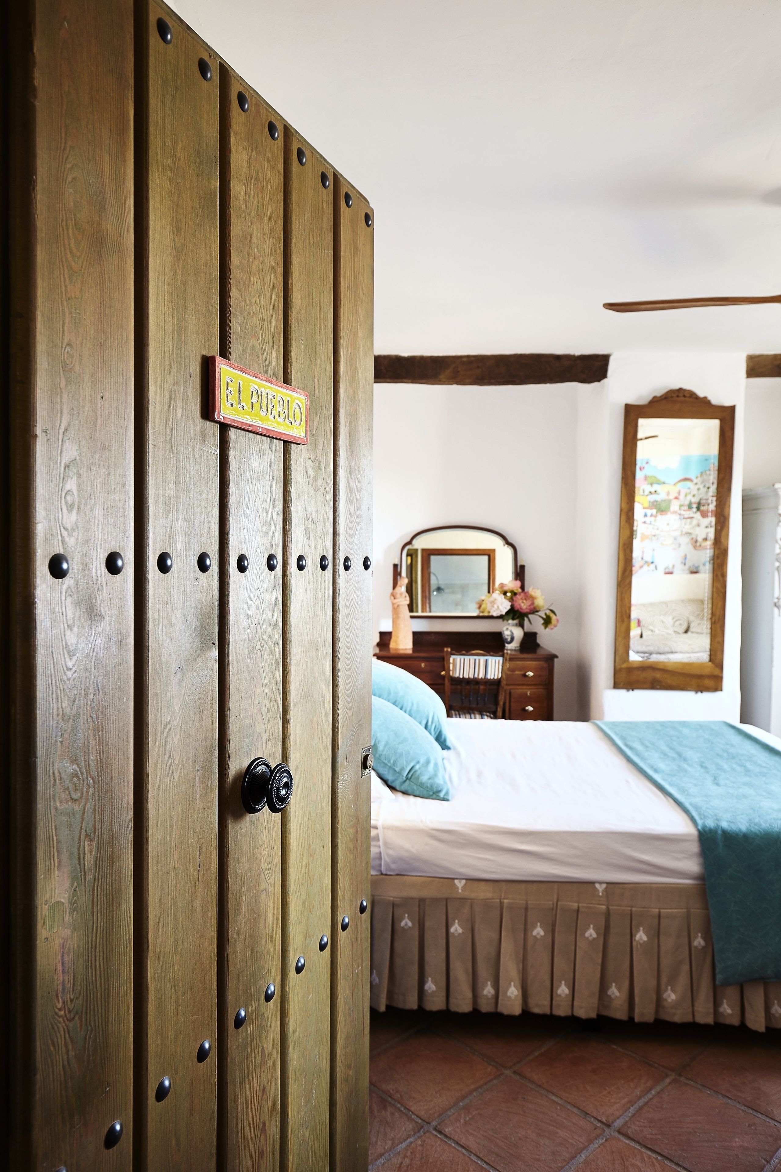 A bedroom with a wooden wardrobe, a bed with a blue blanket, a dresser with a mirror, and a wall-mounted picture.