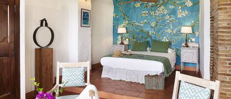 A bedroom with a large floral tapestry, a wooden bed frame, and a view of the outdoors.