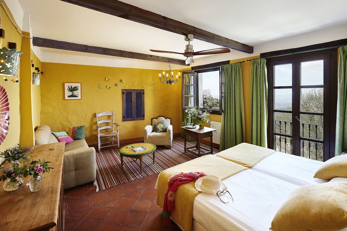 A room with a bed, a chair, a small table, and a window with curtains.