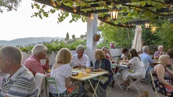 Un grupo de personas cenando al aire libre en una mesa con vistas a las colinas.