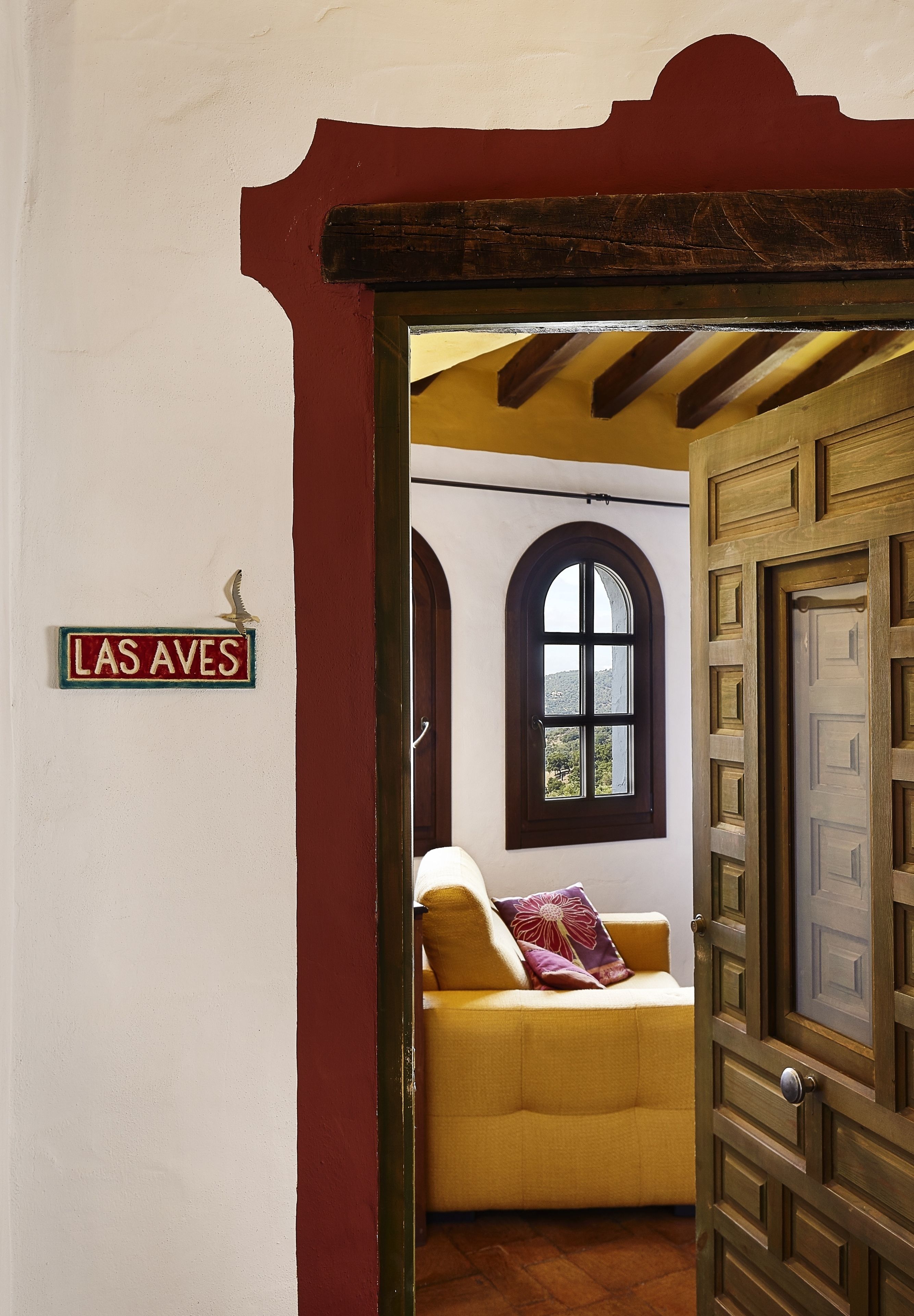 A room with a yellow sofa, a wooden door, and a window with a view.
