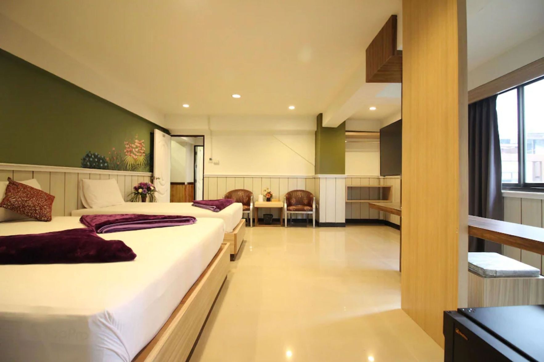 A modern hotel room with a large bed, a small table, a chair, and a view of the city through the window.