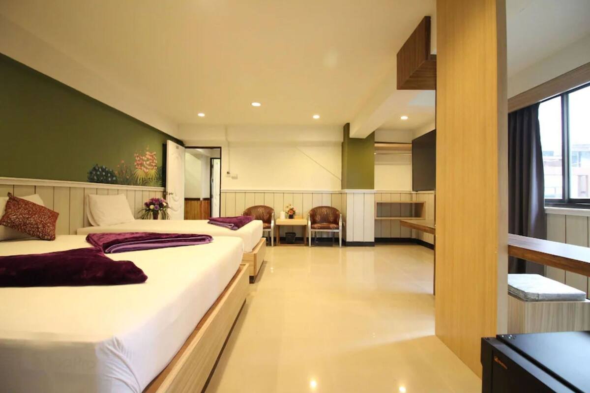 A modern hotel room with a large bed, a small table, a chair, and a view of the city through the window.
