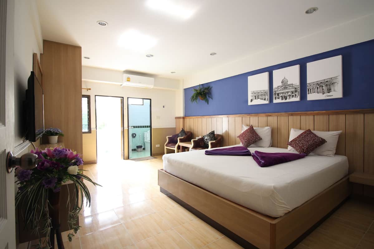 A modern hotel room with a large bed, wooden headboard, and a blue accent wall with framed pictures.
