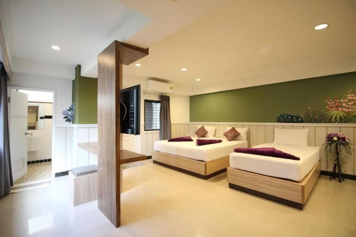 Une chambre d’hôtel moderne avec deux lits, un plancher en bois, un mur d’accent vert et une petite table.