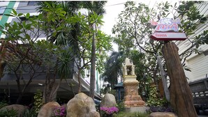 A traditional Thai temple with a stone statue, surrounded by large rocks and flowering plants. - Kaya Place (Bangkok)