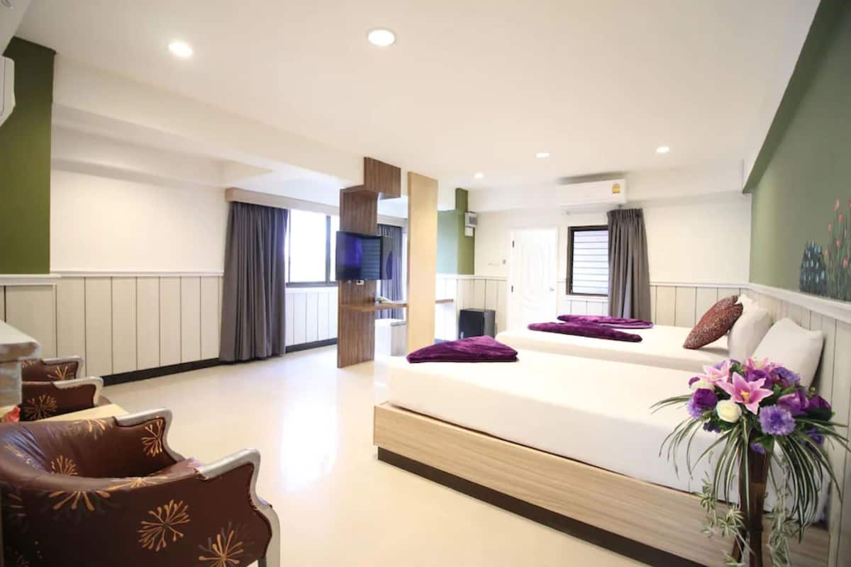 A hotel room with a large bed, a seating area with chairs, a television, and a balcony with curtains.