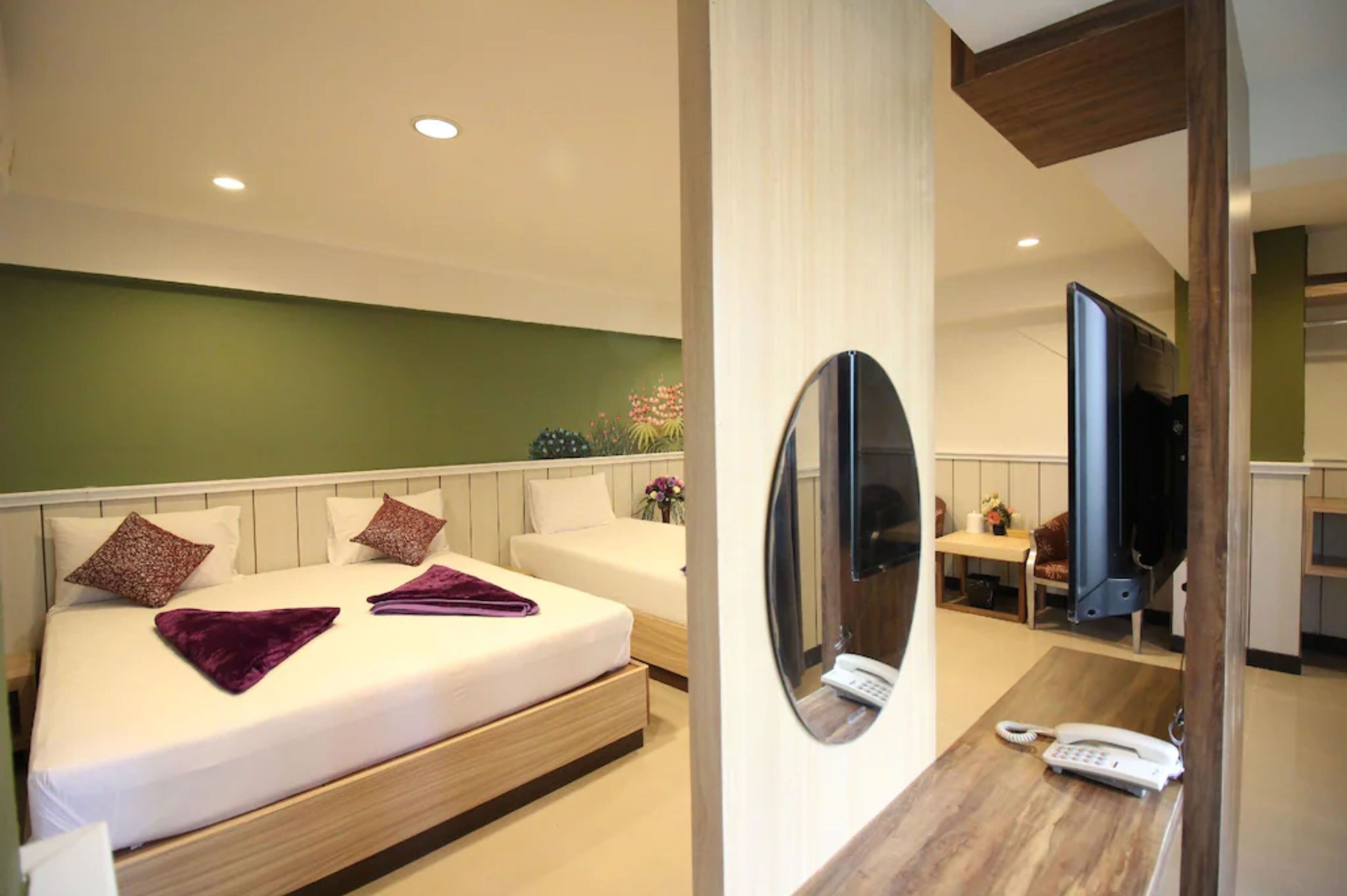 A modern hotel room with a bed, a bedside table with a phone, a mirror, and a TV.
