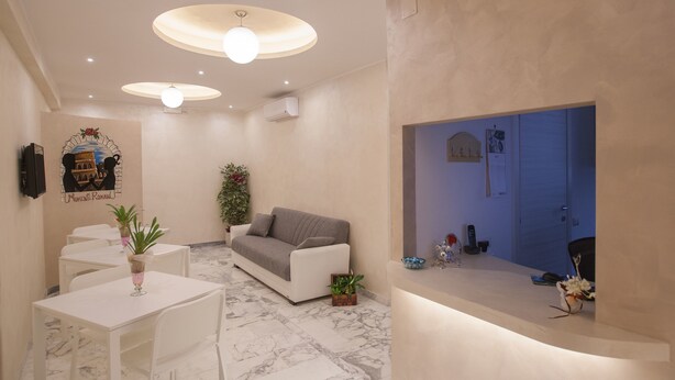 Uma sala de estar moderna com sofá, mesa de jantar e cadeiras. Há uma TV fixada na parede e uma planta decorativa.
